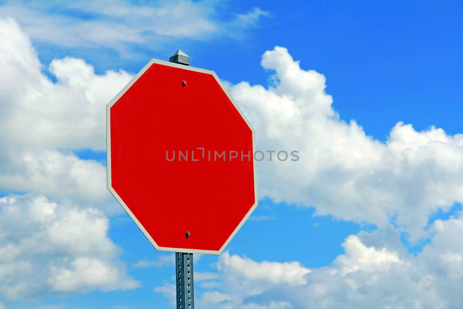 An empty red shield (stop shield) against a blue sky with clouds. An empty red traffic sign