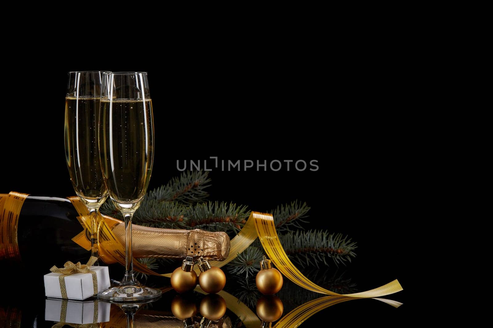 Two wineglasses with champange, bottle, gift box and serpentine on a black background with reflection. Copy space. Christmas and New Year background