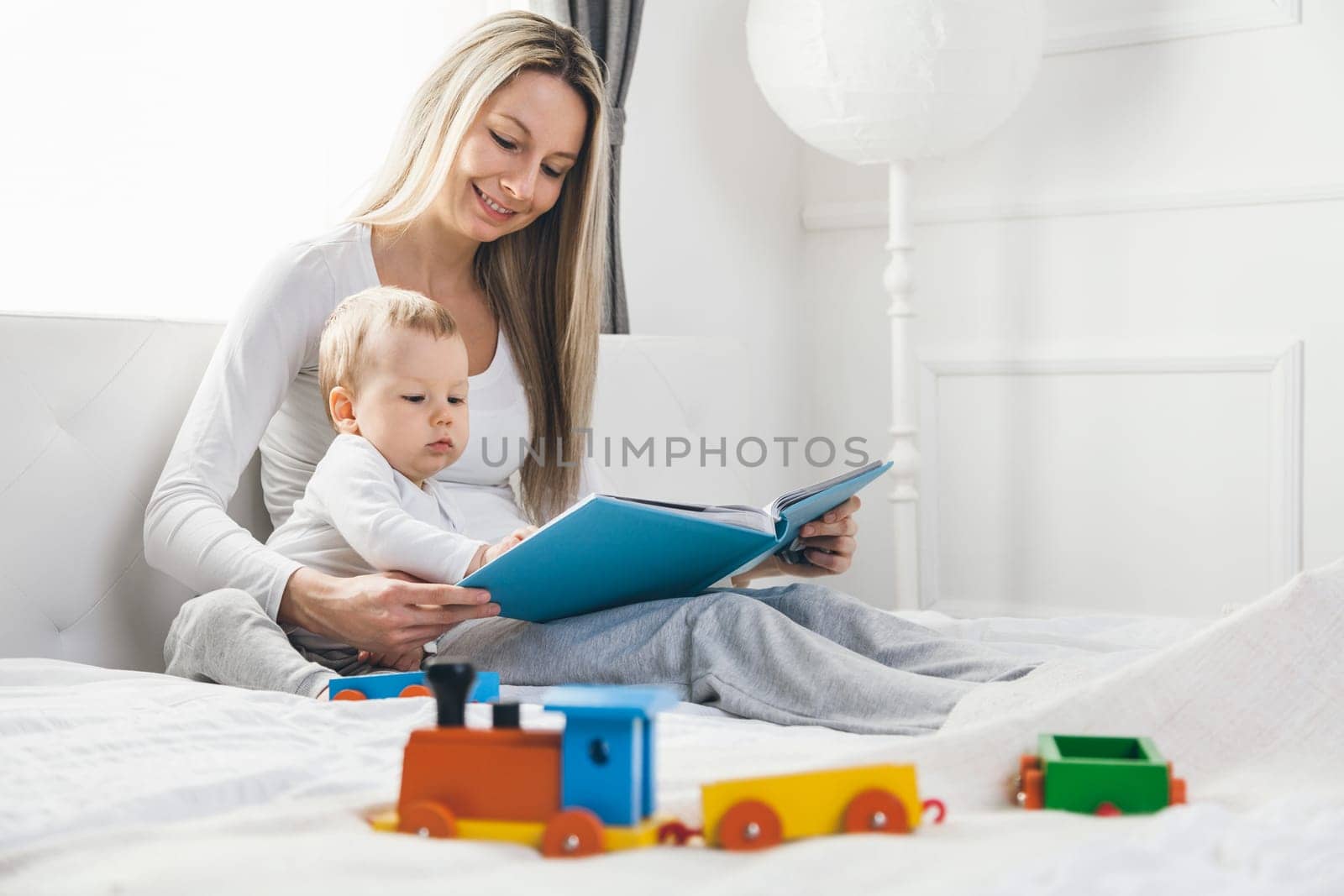 Child education. Happy mother with her toddler sitting on the bed and reading a book together