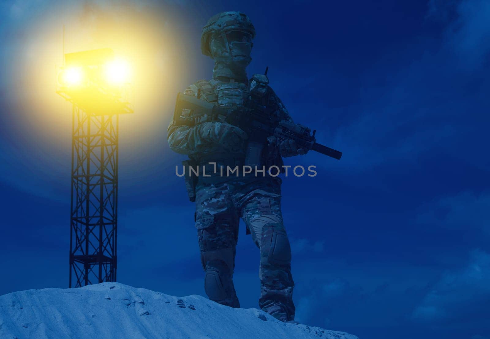 US Military security service serviceman in camo uniform, helmet and mask, armed with assault rifle standing in backlight beam of war watchtower search light. Military base or prison night watch guard