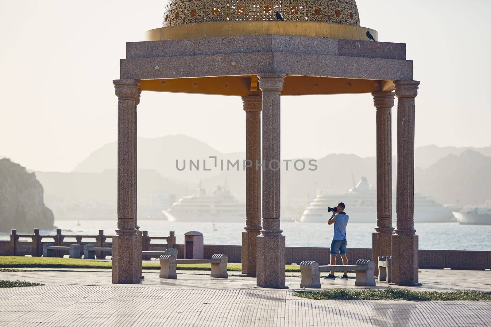 Young tourist photographing waterfront against harbor with modern passenger ships. Mutrah Corniche in Muscat, Sultanate of Oman.