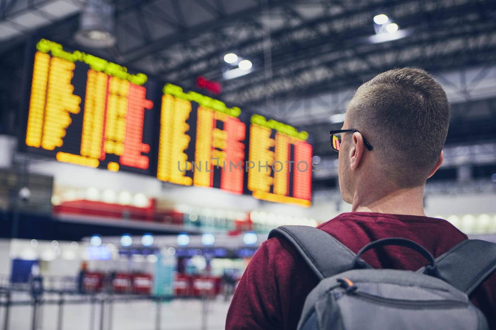 Rear view of young man checking flight schedule on the arrival departure board at airport.