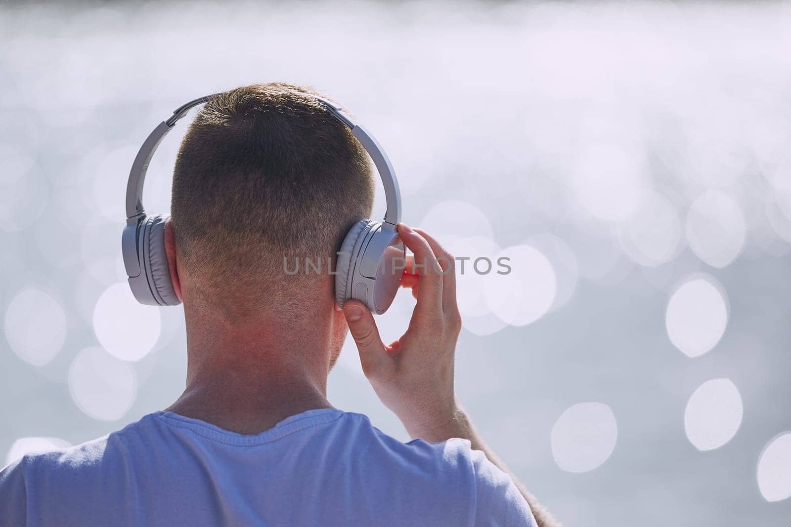 Young man with headphones listening music against bokeh of waves of sea.