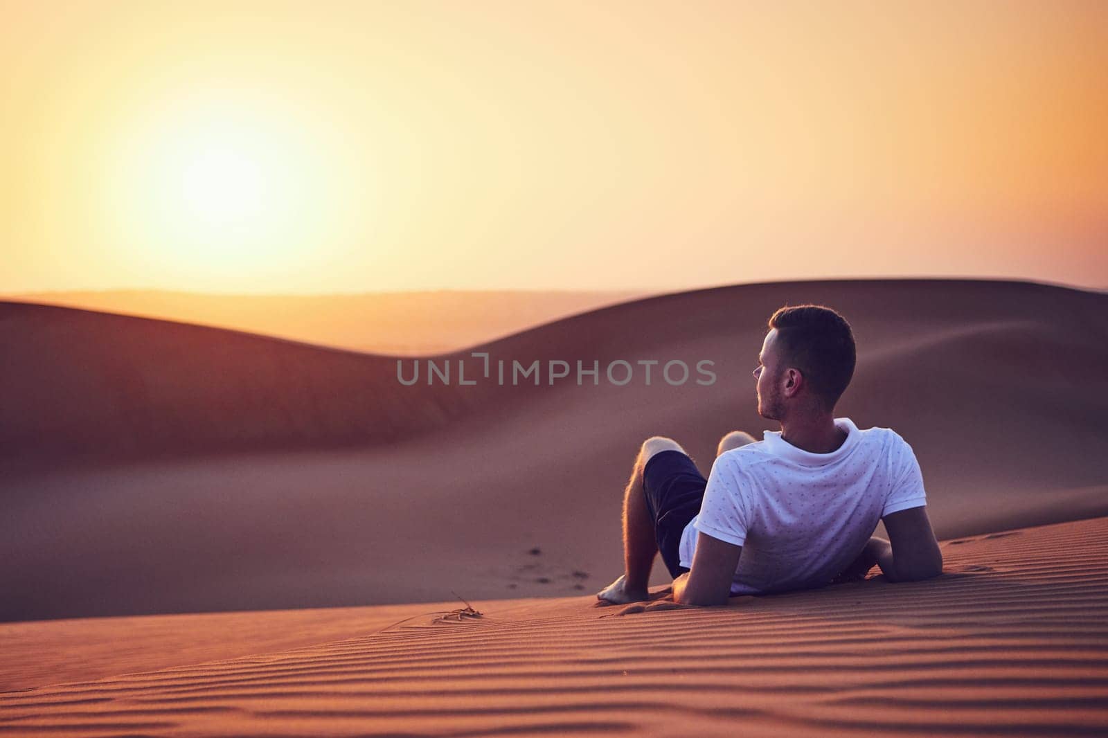 Idyllic sunrise in desert. Young man contemplation on sand dune. Wahiba Sands in Oman.