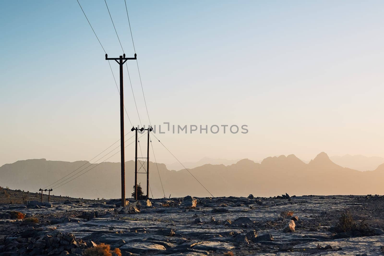 Pylons with power lines in mountains at colorful sunset, Oman