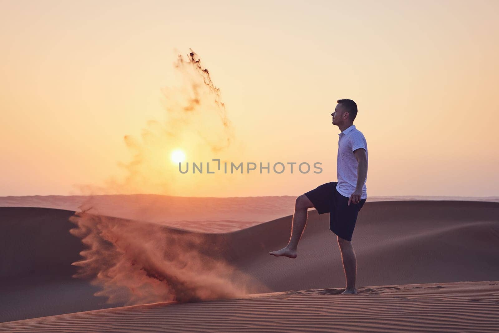 Happy man kicking sand and having fun in desert at sunrise. Wahiba Sands in Oman