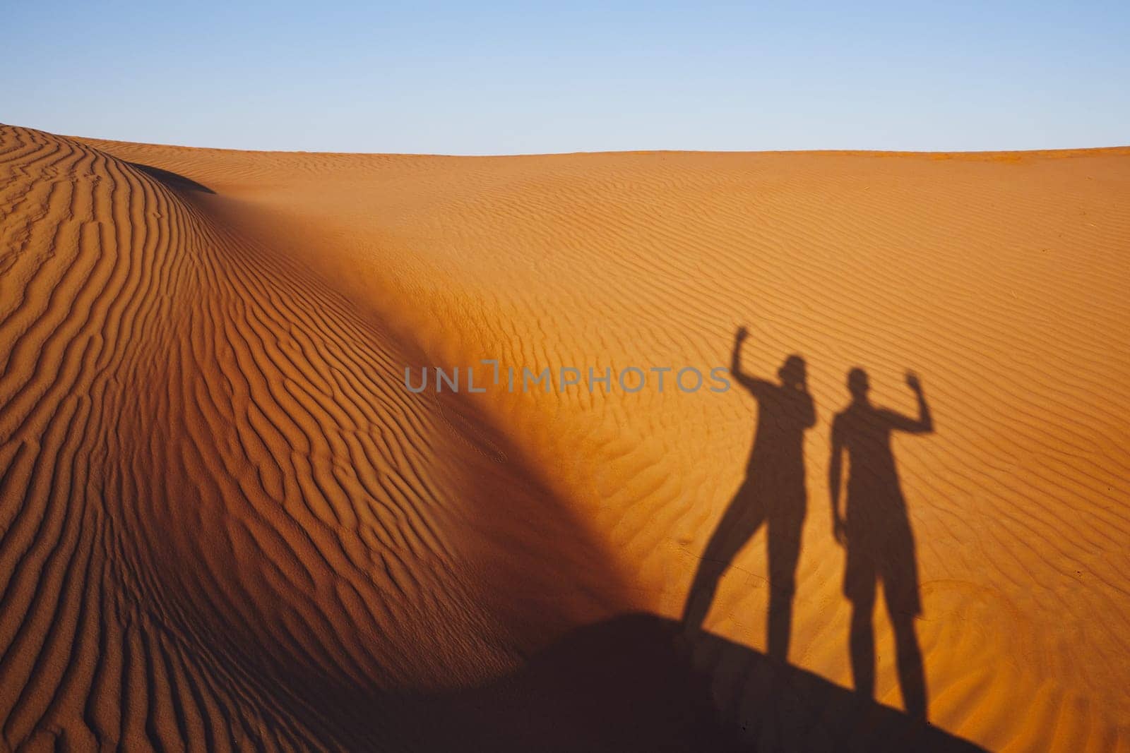 Shadows of two friends waving on greeting. Sand dunes in Oman desert.