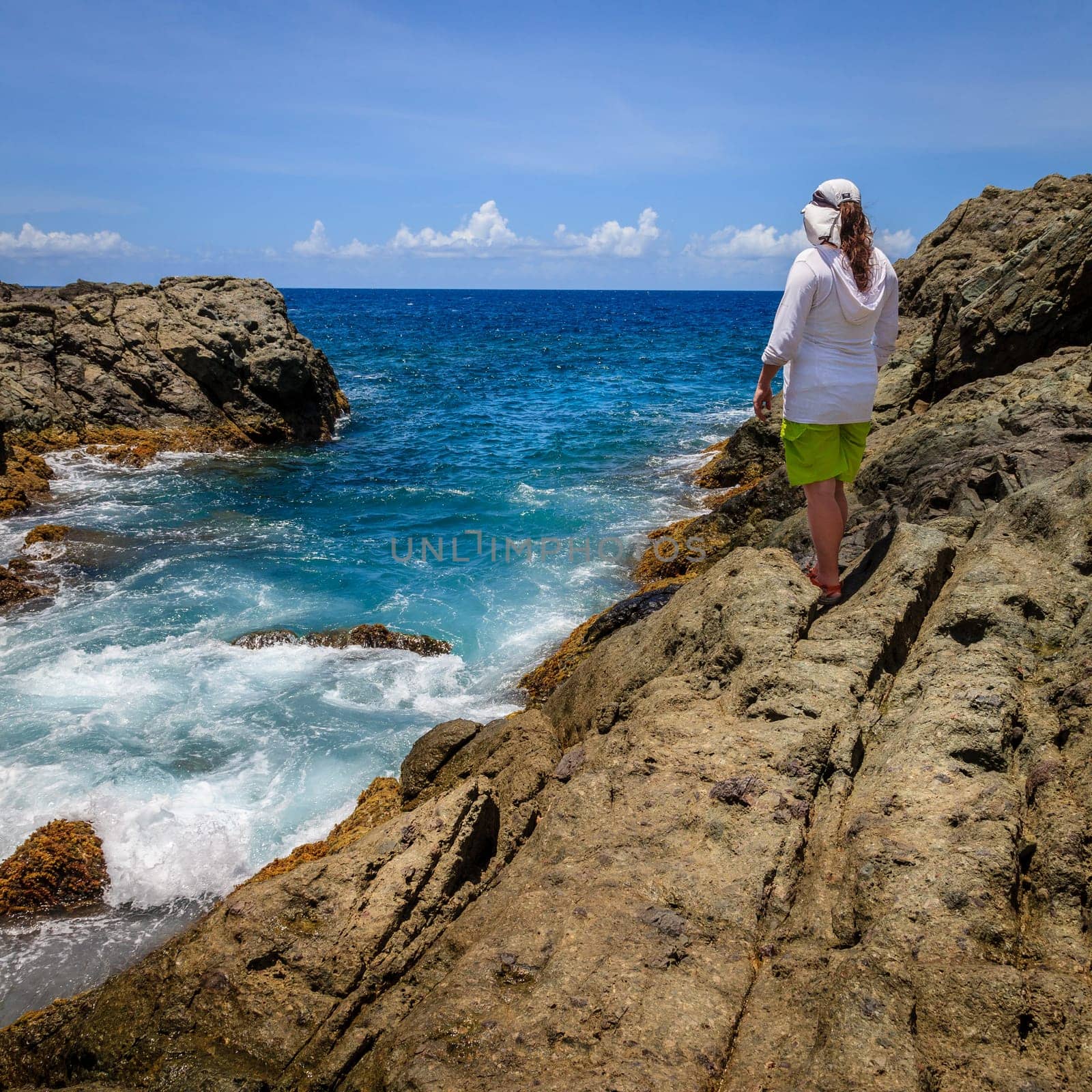 A woman standing on a cliff and watching surf on an island in BVI