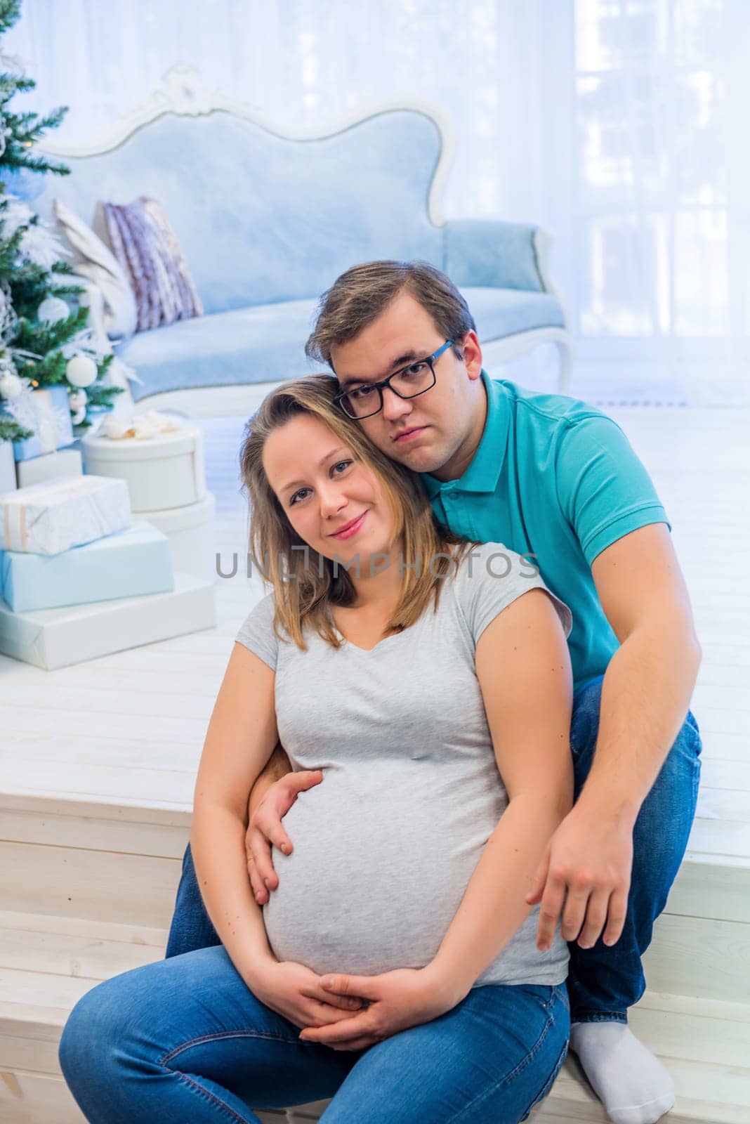 Family portrait near christmas tree. People sitting on the staircase. Pregnant woman