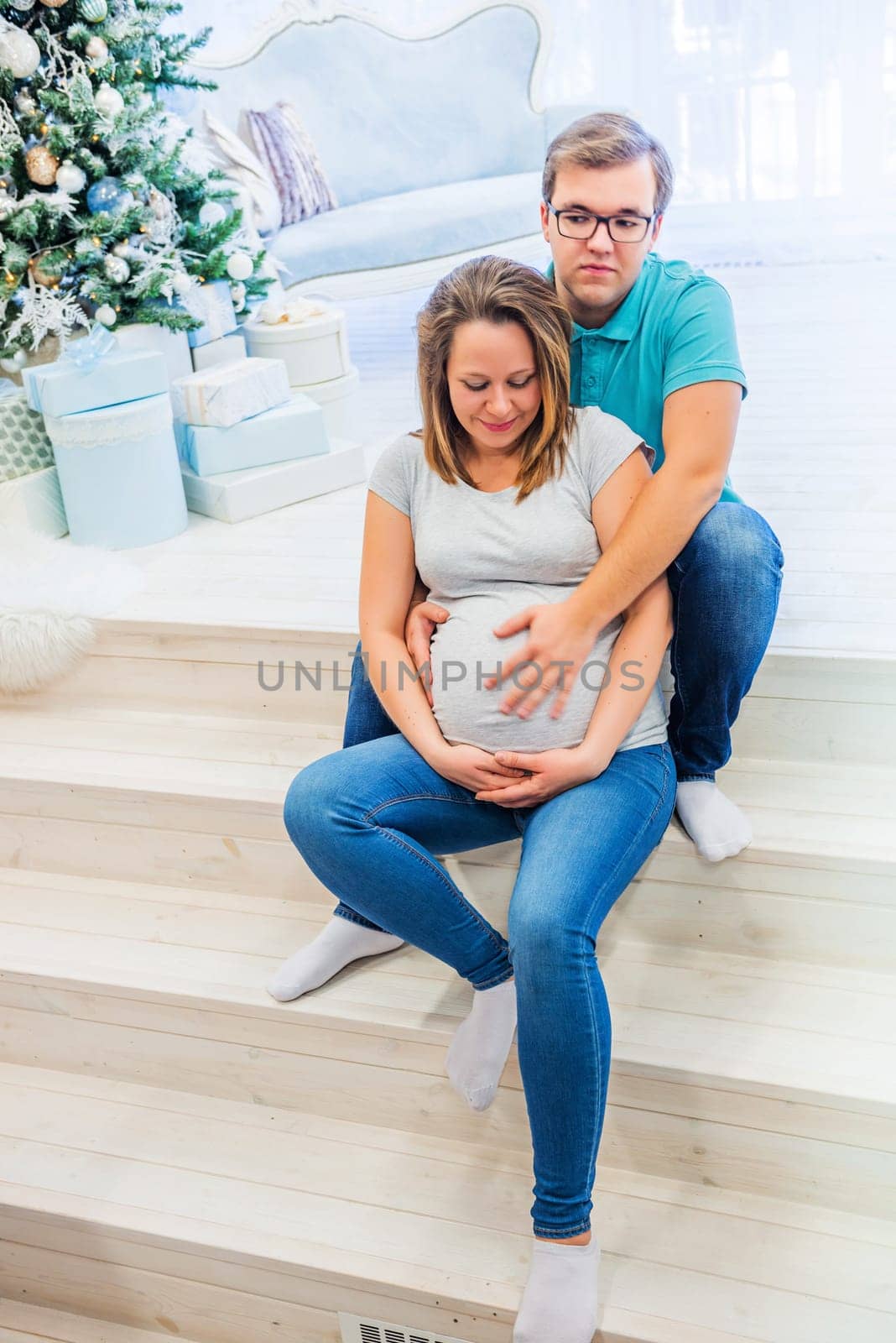 Family portrait near christmas tree. People sitting on the staircase. Pregnant woman