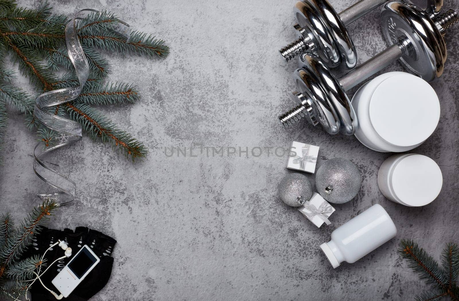 Sports nutrition (supplements), dumbbells, gift boxes, fir tree branches and christmas ornament on a gray background. Top view with copy space. New Year and Christmas. Fitness. Healthy lifestyle.