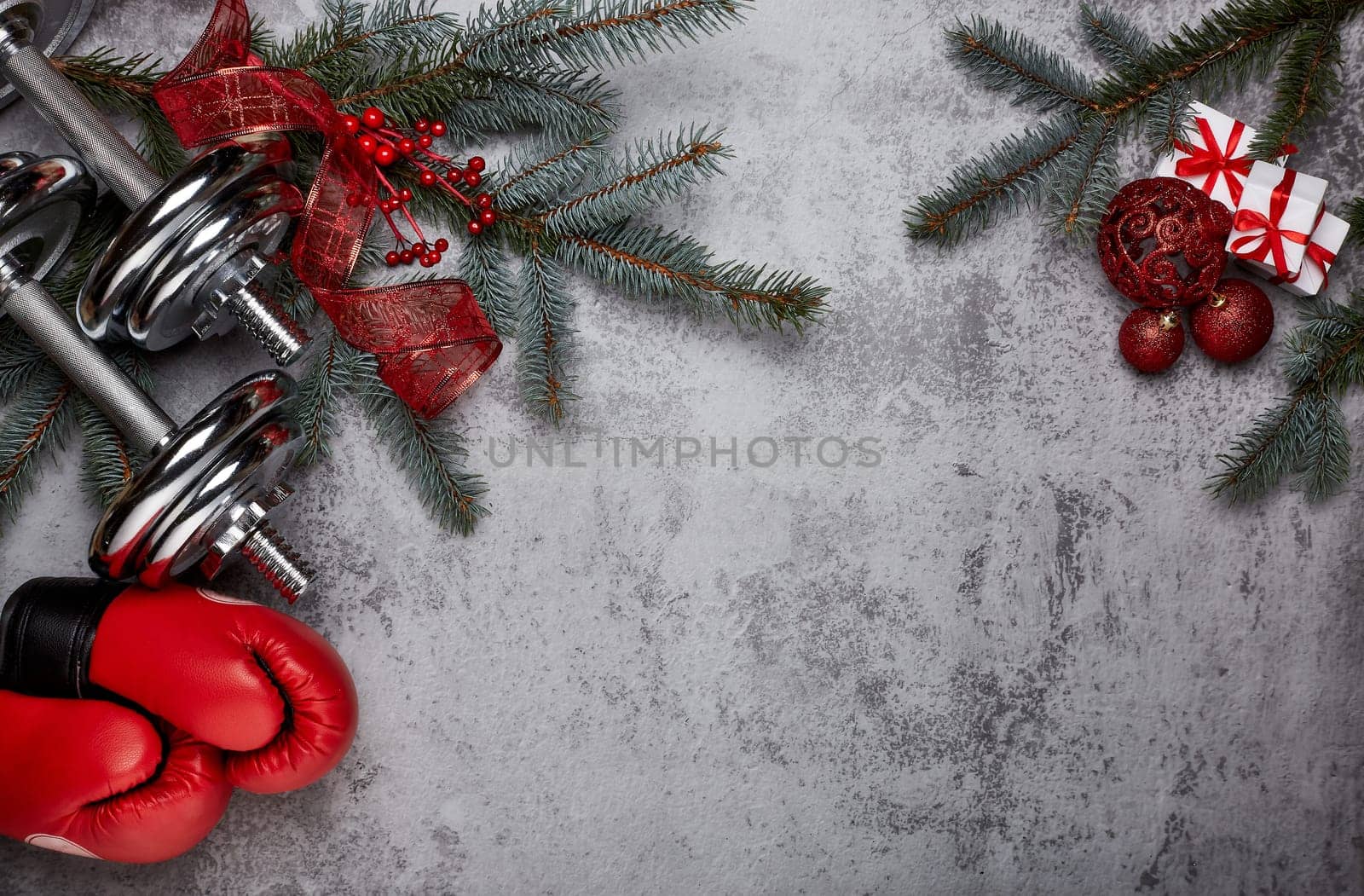 Dumbbells, boxing gloves, fir tree branches and Christmas decorations on a gray background.Top view with copy space. New Year and Christmas. Fitness, sport and healthy lifestyle concept.