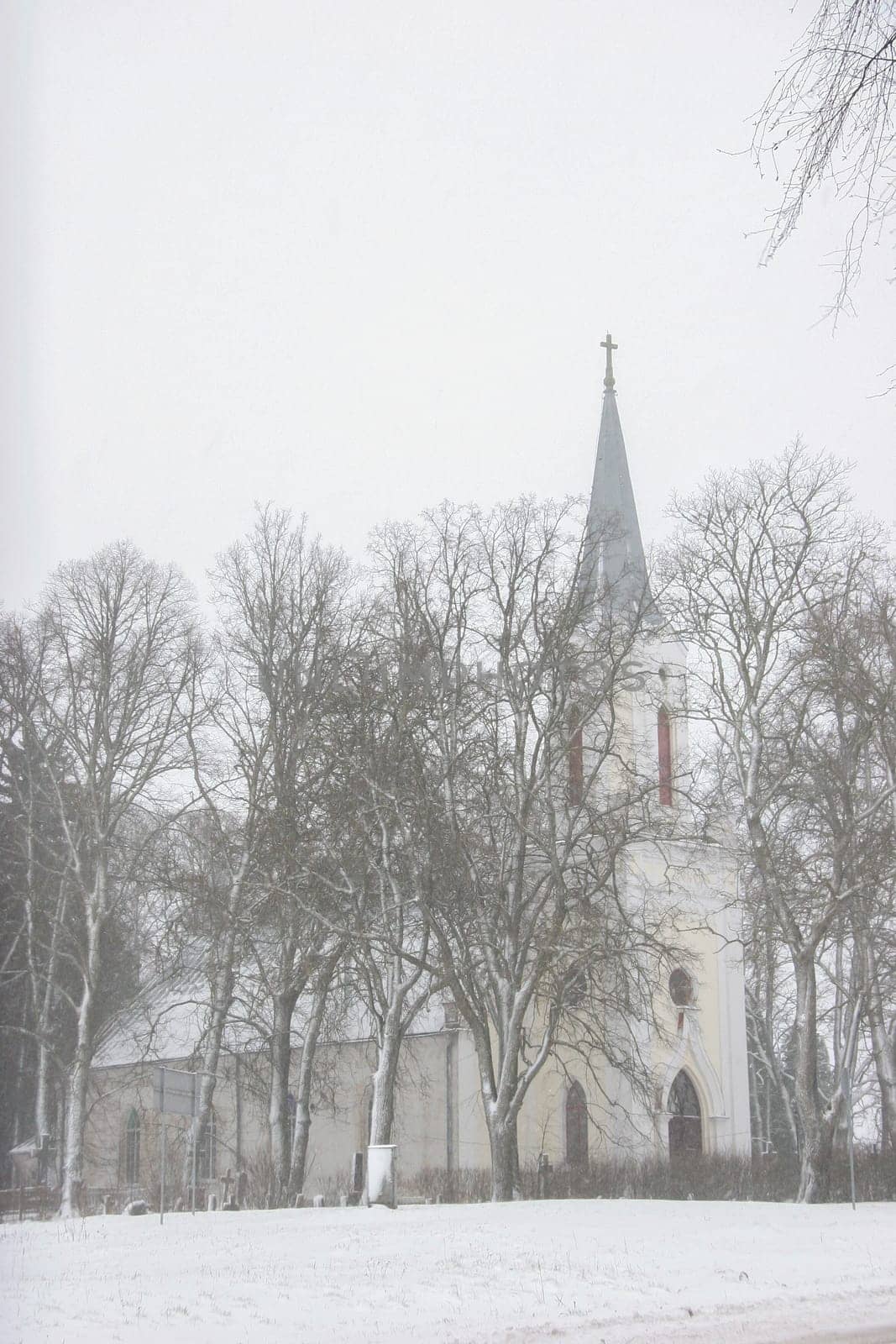 Church in snowfall. Winter in Barbele, Latvia. Church covered in snow. Winter landscape with snow covered church and trees...