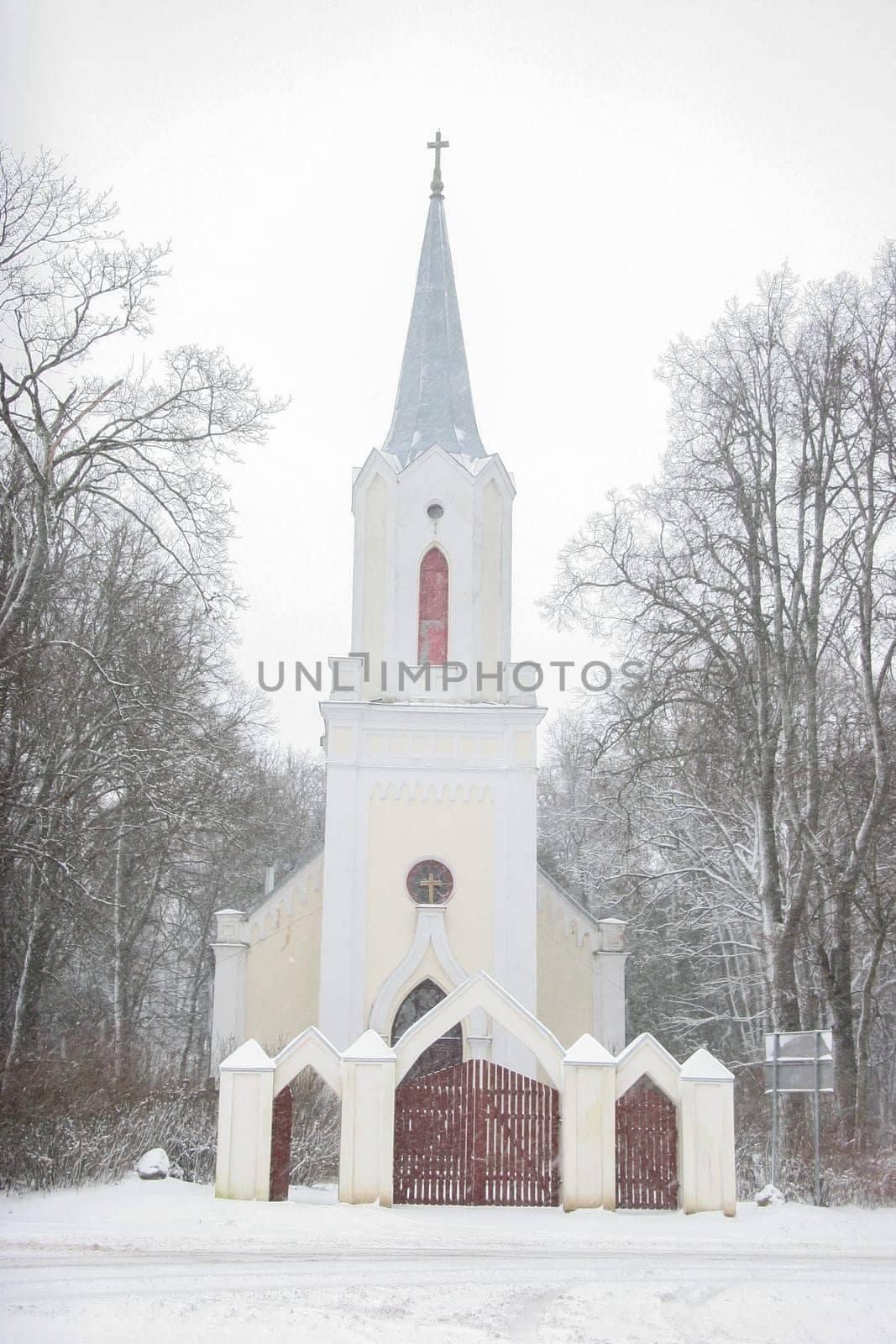 Church in snowfall. Winter in Barbele, Latvia. Church covered in snow. Winter landscape with snow covered church and trees.....