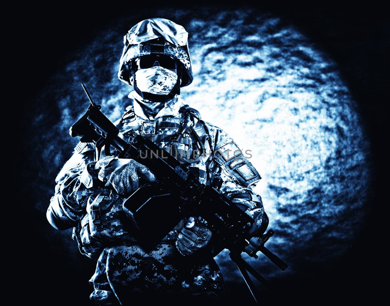 United States Marine Corps soldier in camouflage protective ammunition with hiding identity, armed with machine gun blue tone studio shot. Army infantry posing with weapon, spotlight in background