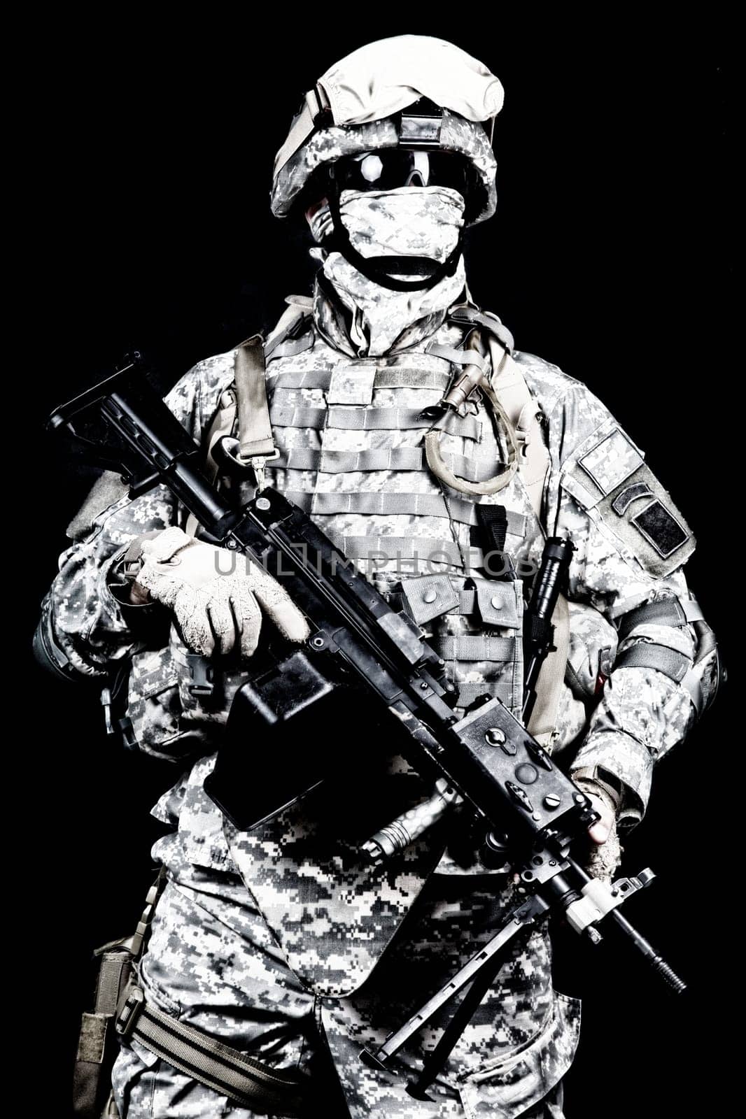 Marine with hiding identity, protected with helmet and body armour in digital camouflage combat uniform posing with light machine gun equipped infrared laser aiming light isolated on black background
