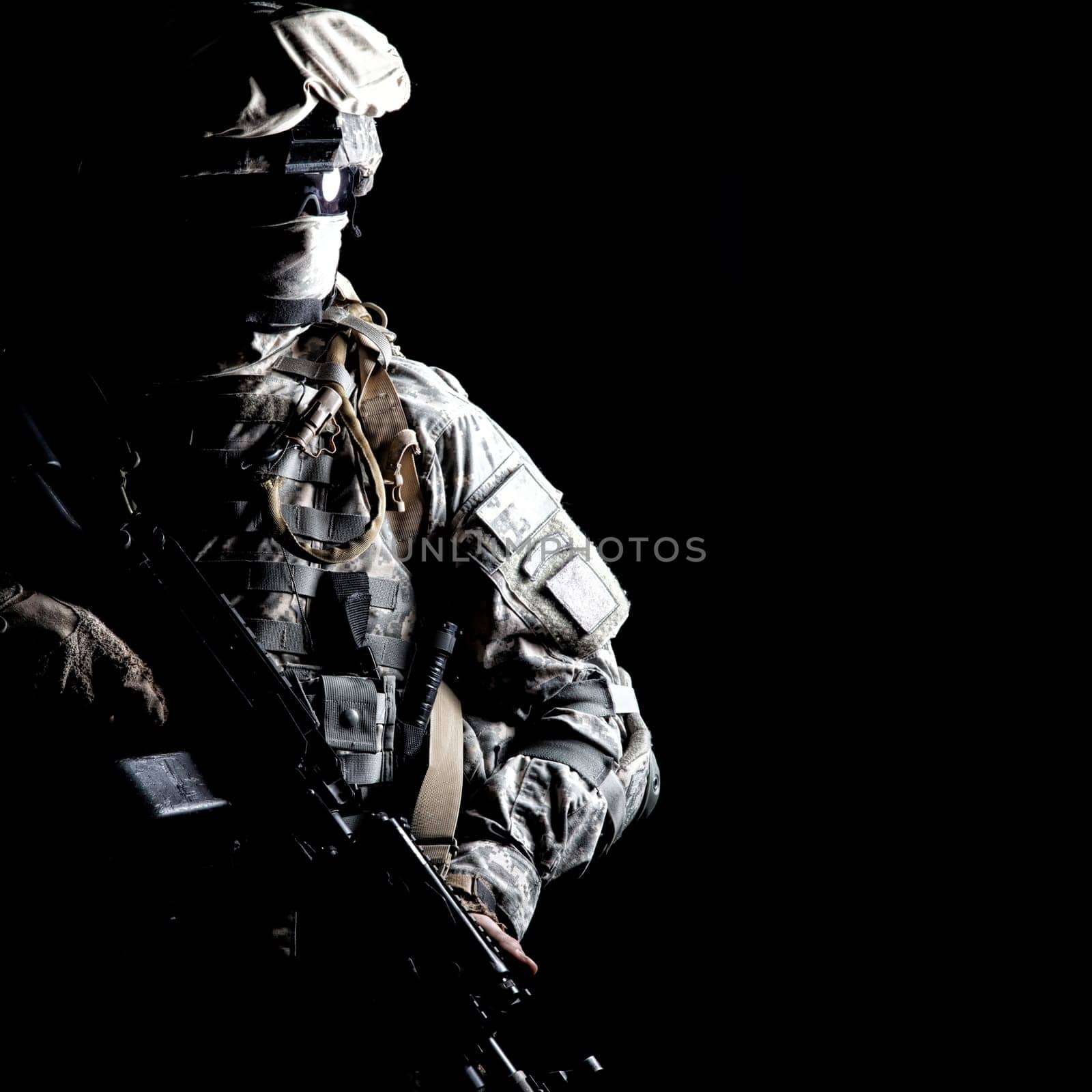 Armed army soldier in camouflage uniform, with hidden face, sneaking in dark during combat, counter terrorist raid. Secret military operation, stealth mission under cover of darkness, night patrol