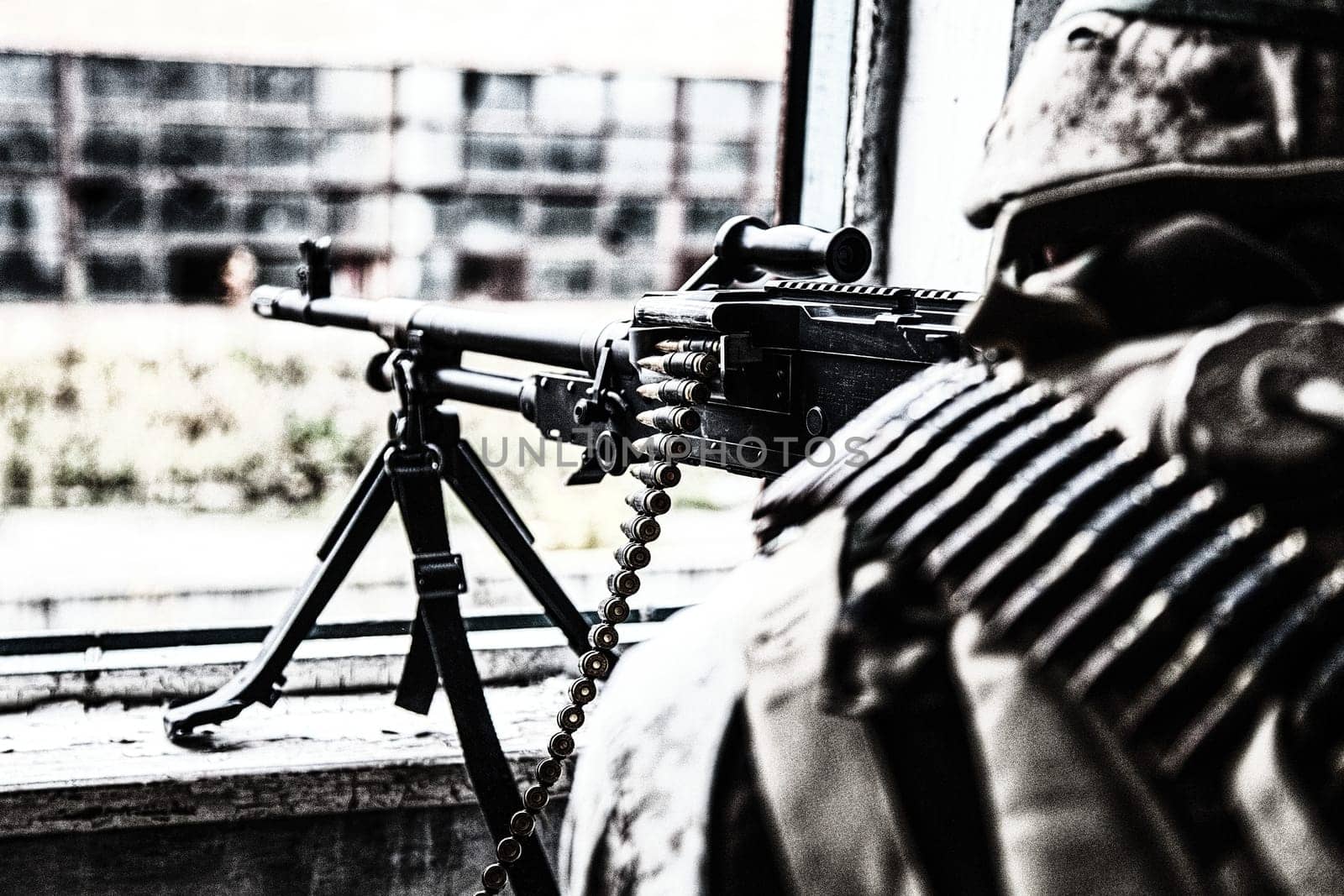 Commando machine gunner, U.S. Marine Corps infantryman, military squad automatic weapon operator in helmet and ammo belt around body, firing through window in ruined building, over shoulder back view