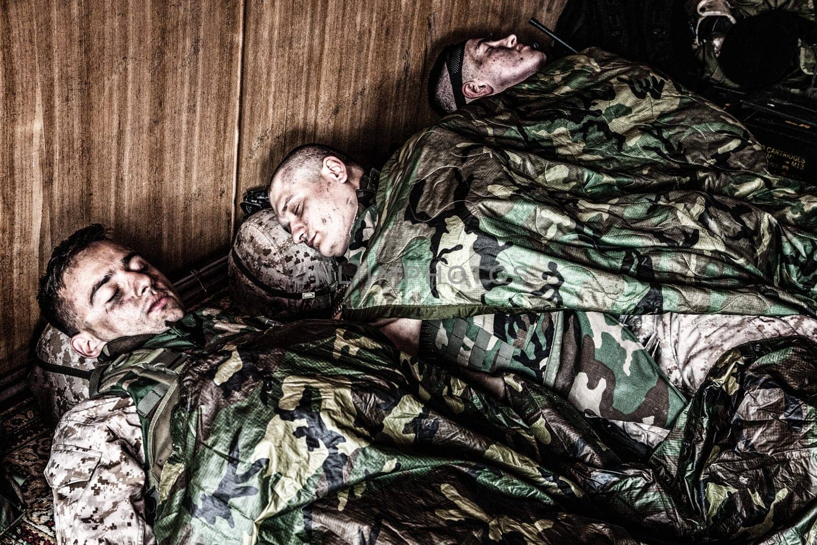 Tired U.S. marines resting at temporary base or camp, lying on floor in uniform and tactical ammunition, covered with poncho liners and sleeping bags, sleeping well after hard raid, exhausting mission