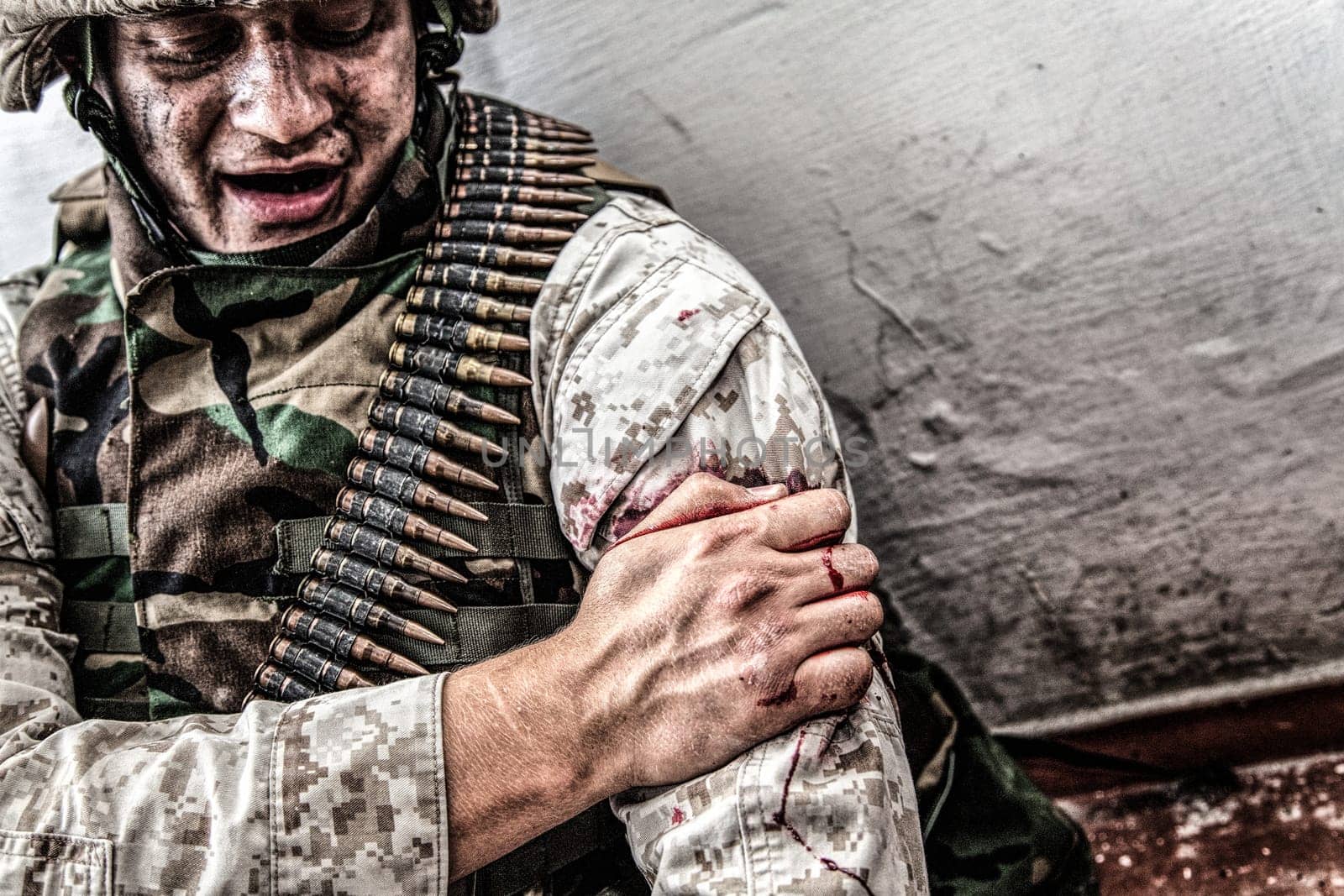 Army soldier, commando fighter, marine machine gunner wounded in shoulder, clamping wound with healthy hand. Infantryman with gunshot wound in upper limb, trying stop bleeding, waiting for medical aid