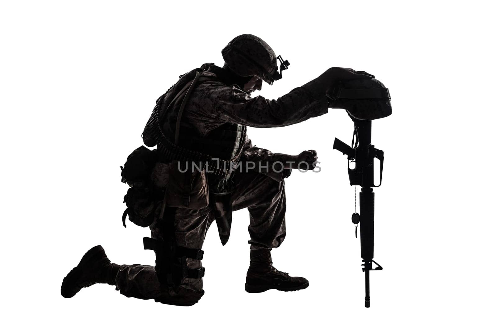 Army soldier in sorrow for fallen comrade, standing on knee, leaning on rifle with helmet and two dog tags on chain, studio shoot isolated on white low key silhouette. Military funeral honors, grief for killed in action