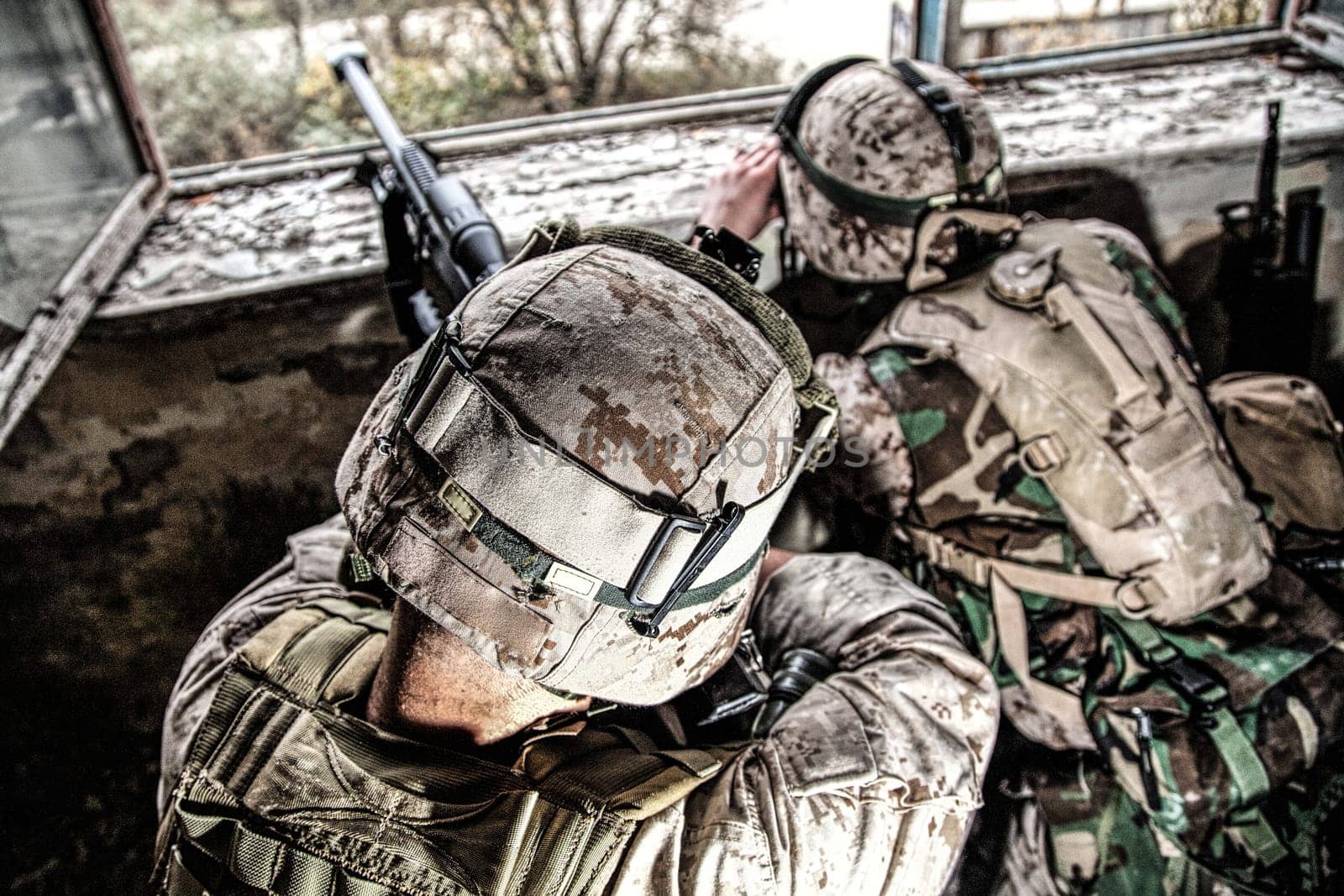 Marines sniper team armed with large caliber, anti-materiel sniper rifle hiding in ruined urban building, shooting enemy targets on range from shelter, sitting in ambush. Military firefight in city