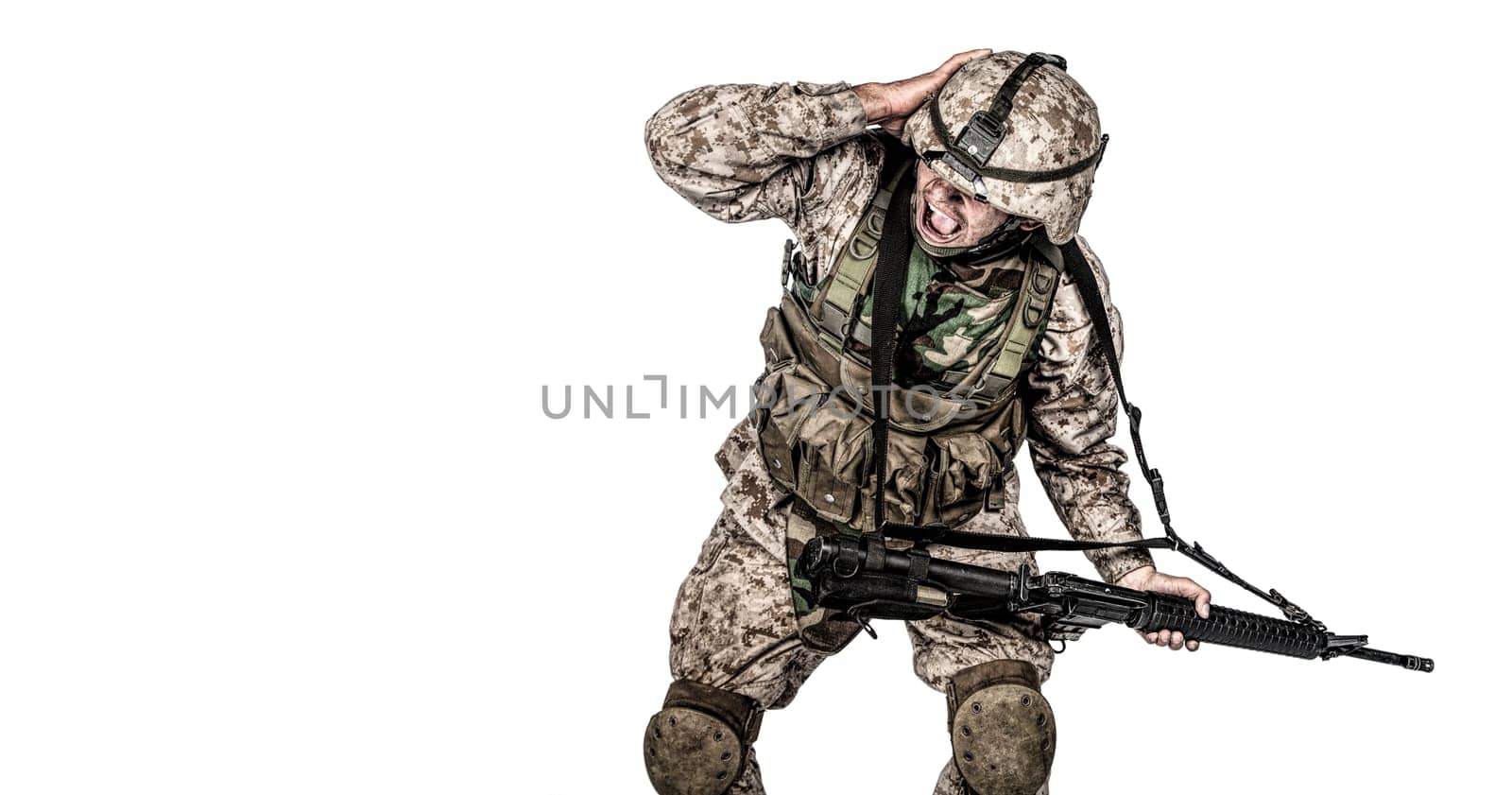 Army soldier in camo uniform, armed with assault rifle and machine gun, crouching to ground, holding helmets and covers ears with hands isolated on white studio shoot Grenade or bomb explosion