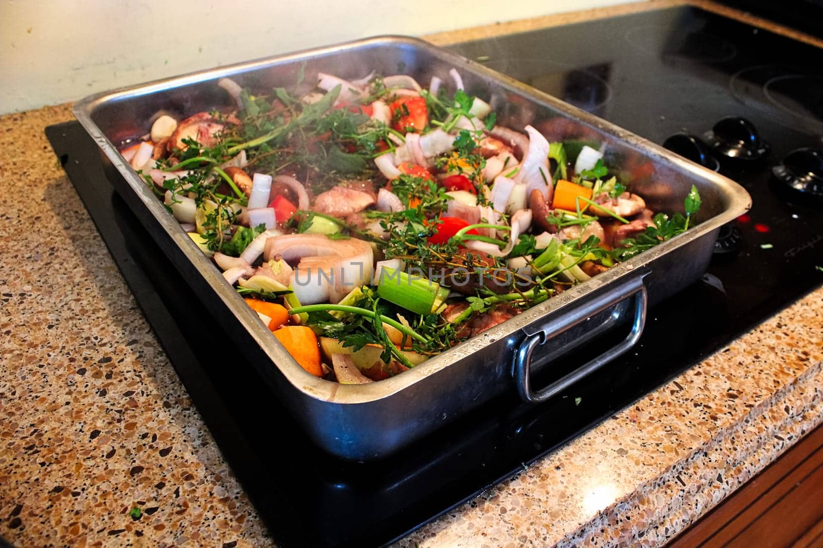 A roasting pan full of vegetables and herbs steaming.