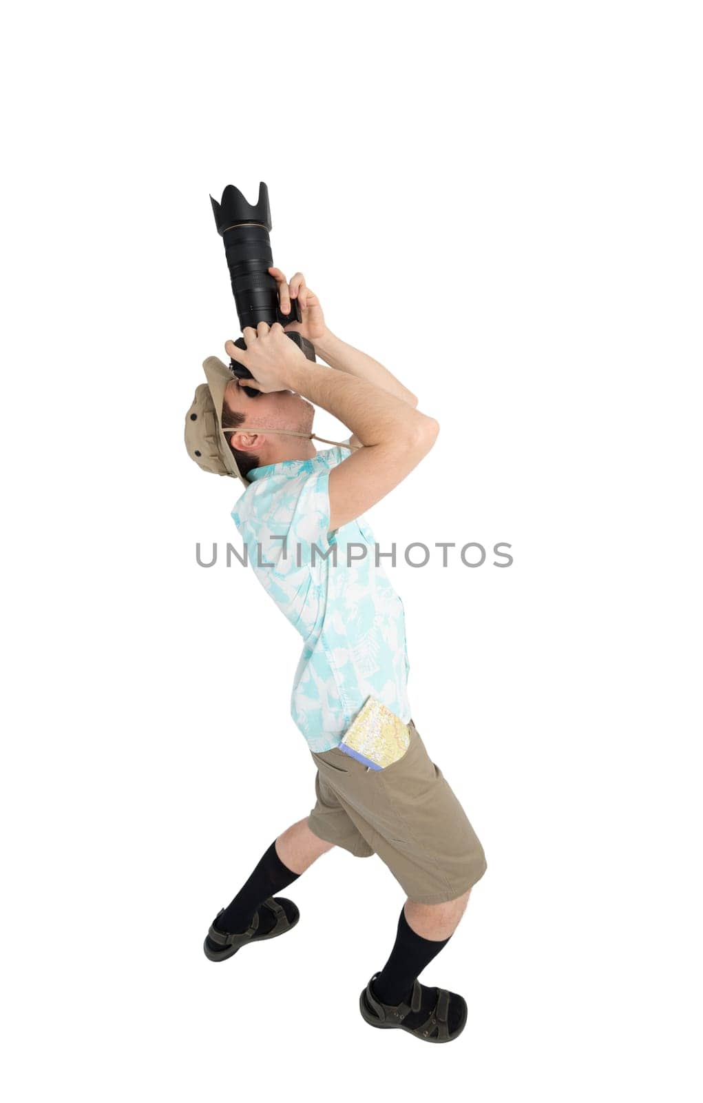 Silly man tourist in blue shirt, black sandals and hat holding big dslr camera and shooting. Traveler concentrating and making pictures. Isolated on white background.