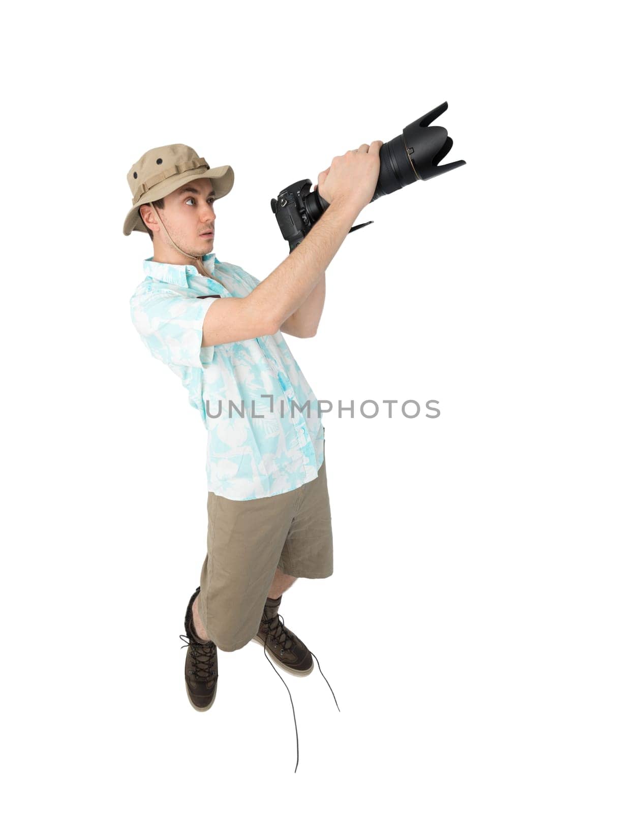 Silly man tourist in blue shirt, brown shorts and hat holding big dslr camera and shooting. Traveler concentrating and making pictures. Isolated on white background.