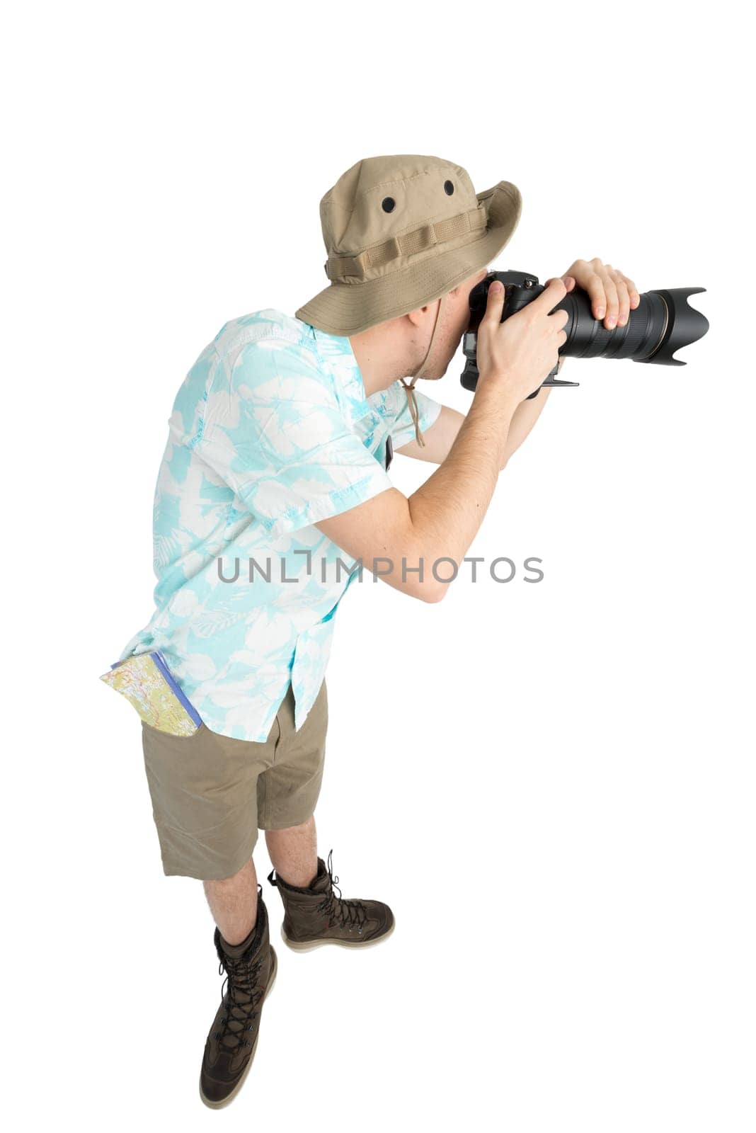 Silly man tourist in blue shirt, brown shorts and hat holding big dslr camera and shooting. Traveler concentrating and making pictures. Isolated on white background.