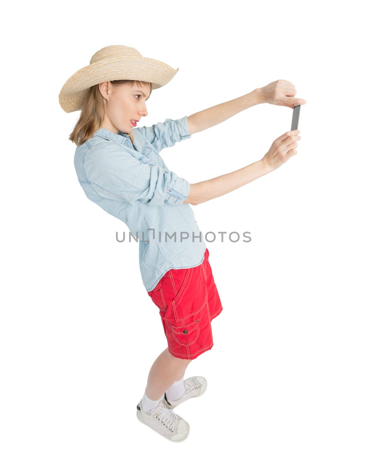 Happy lady tourist in blue shirt red shorts and straw hat makes picture by phone. Isolated on white background. Traveler has Interesting trip on summer vacation.