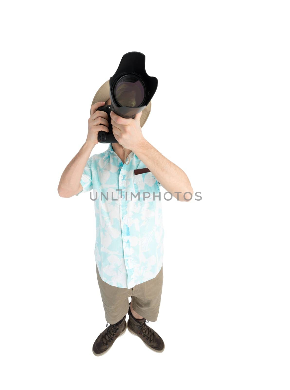 Silly man tourist in blue shirt, brown shorts and hat holding big dslr camera and shooting. Traveler concentrating and making pictures. Isolated on white background.