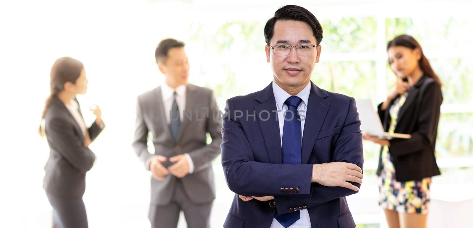 Portrait of asian businessman with business team in background at office window using for coporate working background, panoramic web banner composition