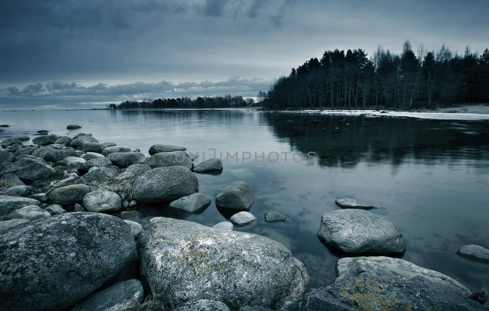 Seacoast in march with stones on the foreground on cloudy evening