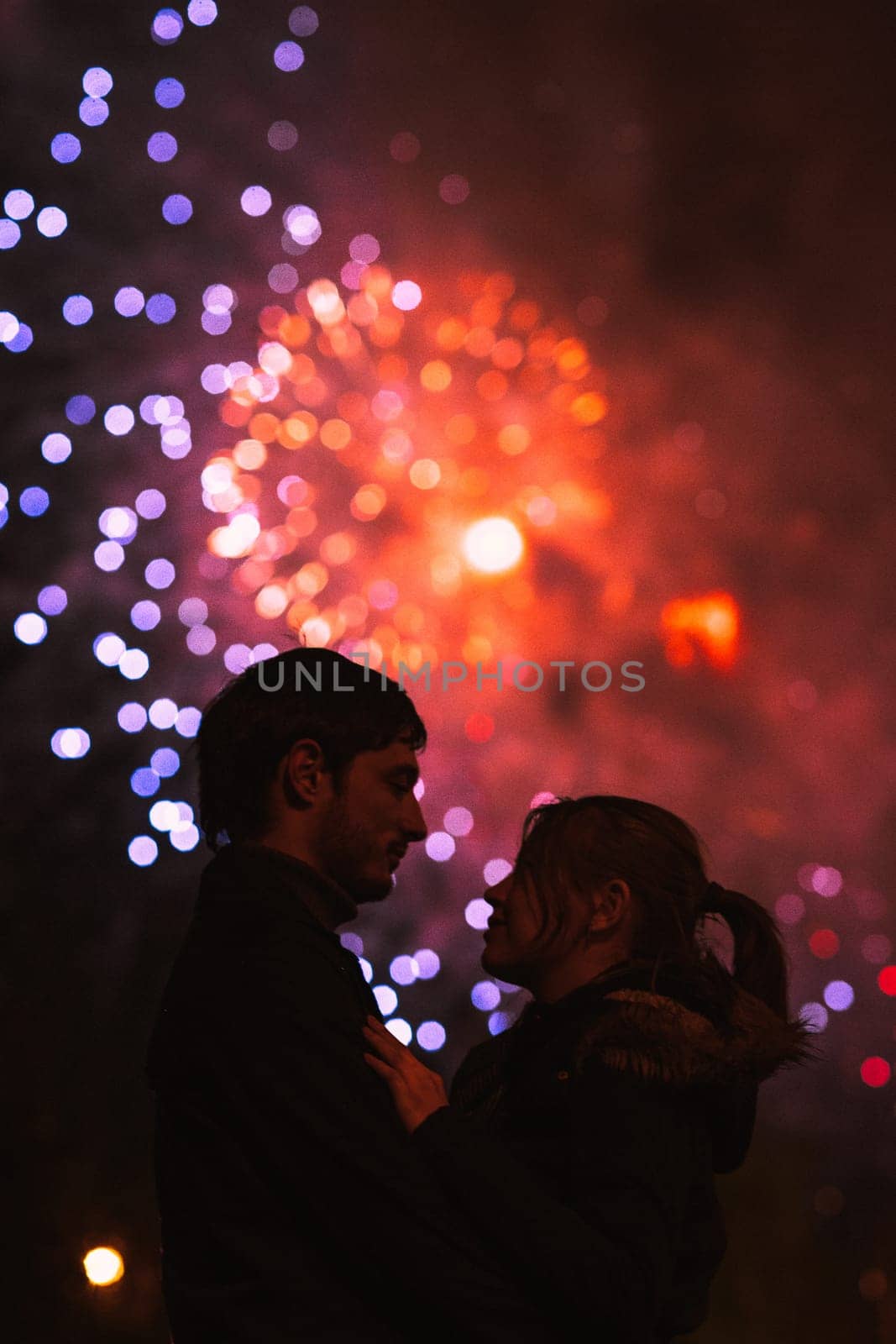 A silhouette of a kissing couple in front of a huge fireworks display. Filtered image with grain