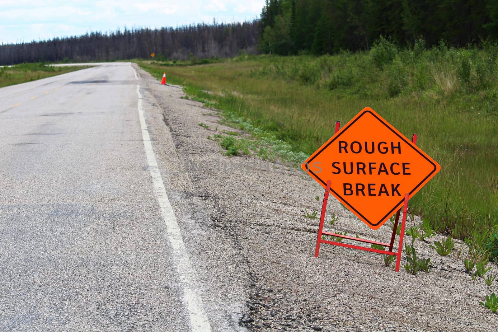 An orange rough surface break sign with a road into the distance.