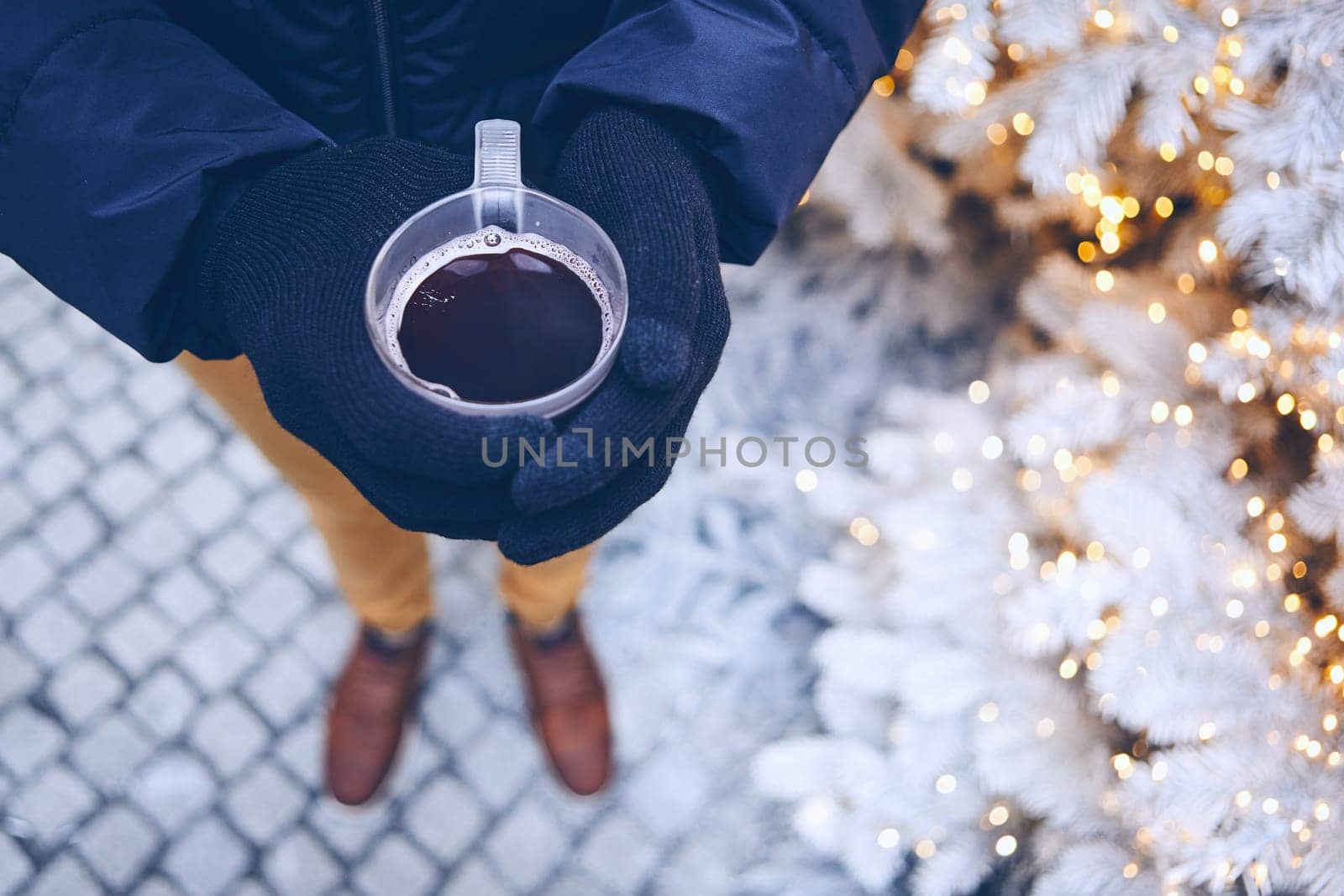 Man holding cup of mulled wine against illuminated christmas tree.  Munich, Germany.