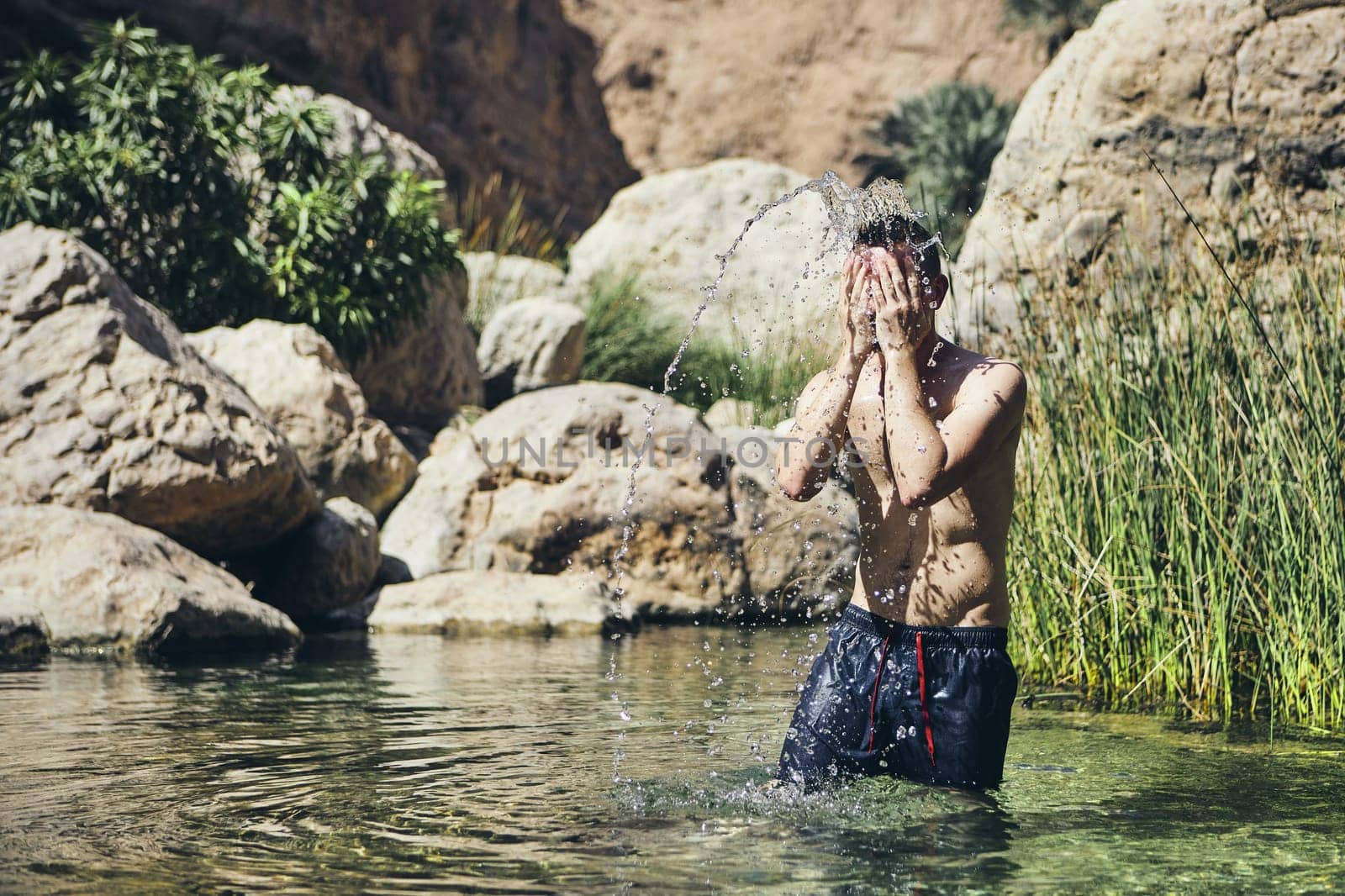 Young man splashing water on face. Refreshing in Wadi Shab, Sultanate of Oman.