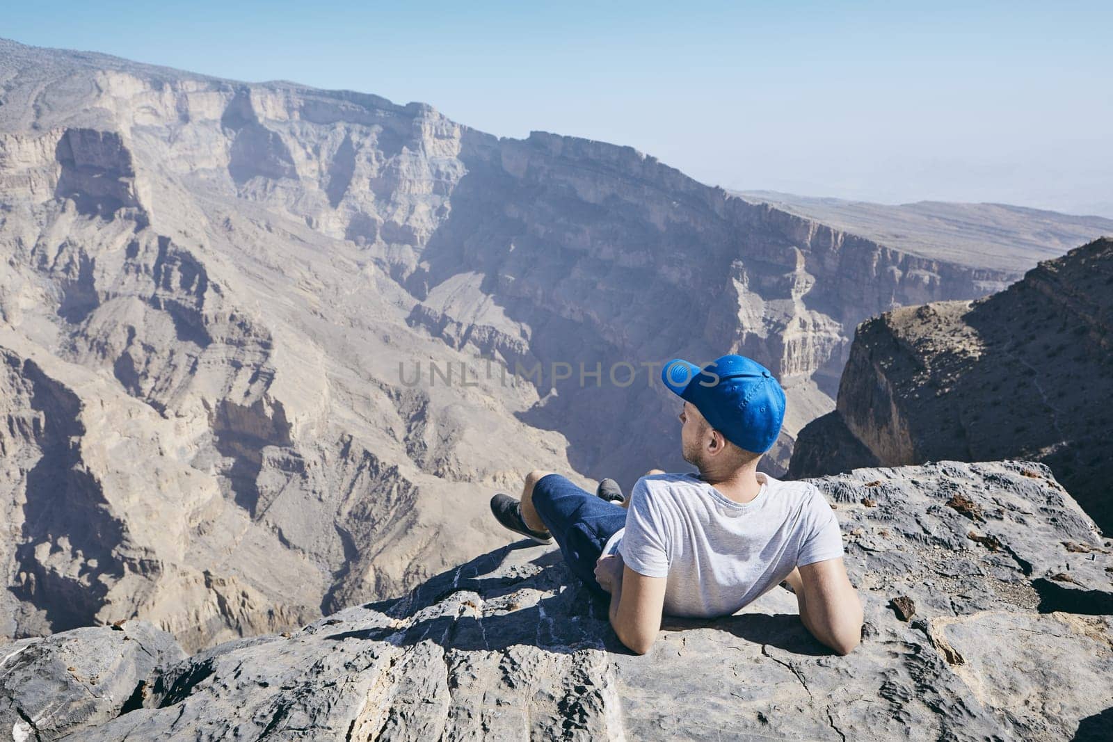 Young tourist resting on the edge of cliff. Jebel Akhdar, Grand Canyon of Oman.