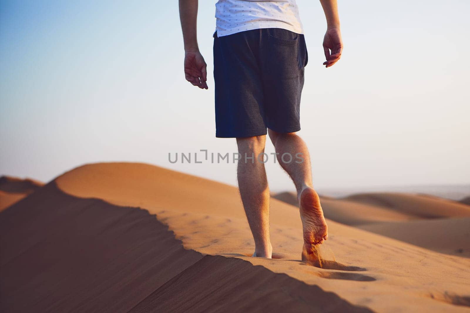 Young man walking on top of sand dune. Wahiba Sands in Oman.