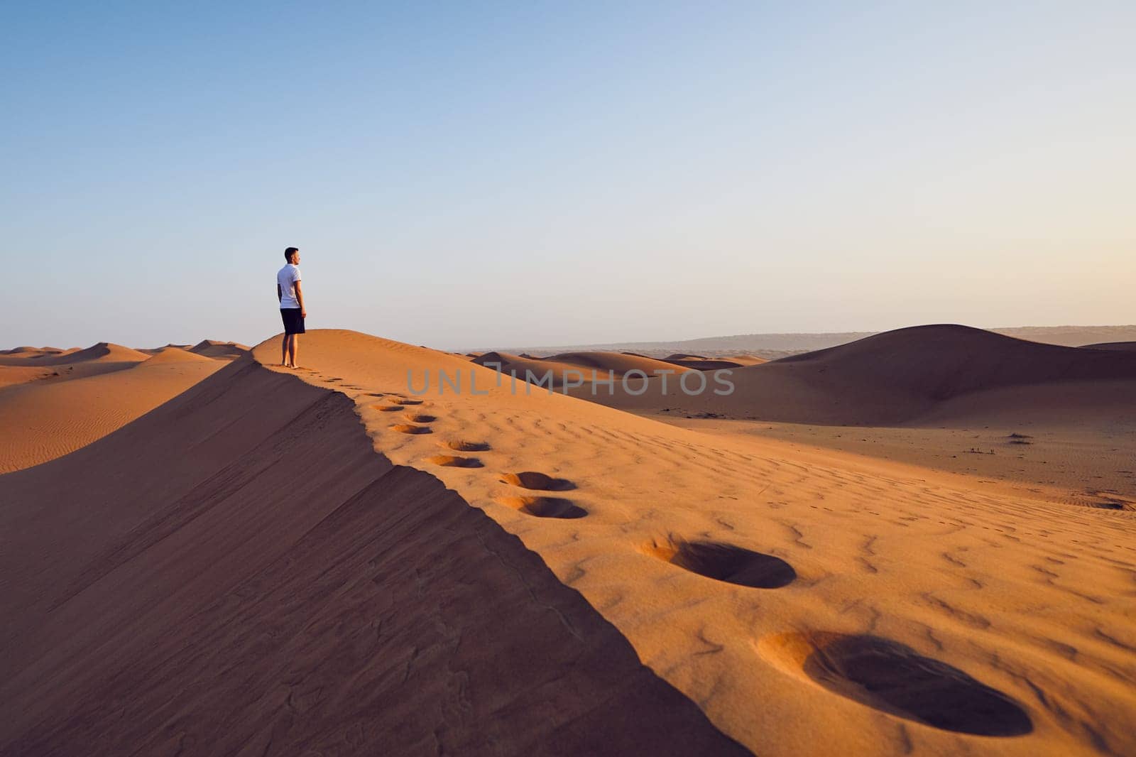 Young man standing on top of sand dune and looking at view. Desert Wahiba Sands in Oman.