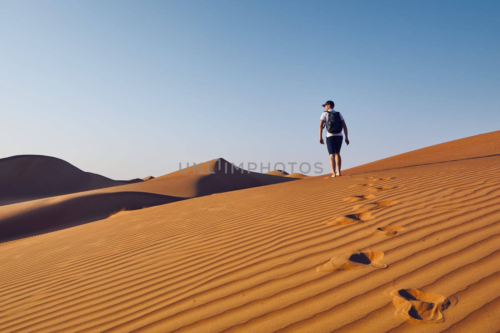 Young tourist with backpack walking on sand dune. Desert Wahiba Sands in Oman.