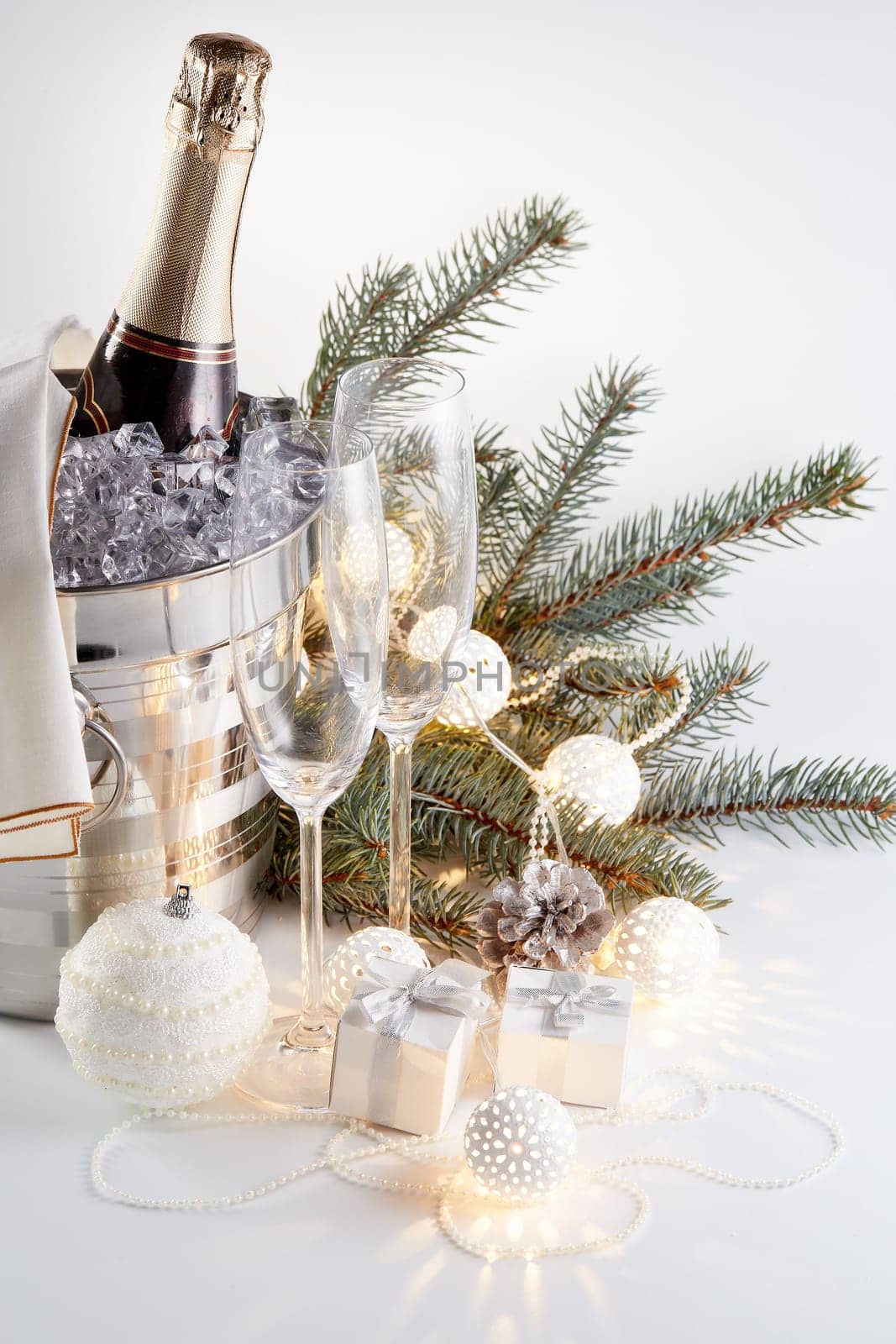 Still life with cooled champagne bottle standing in a bucket with ice, two champagne flutes and Christmas ornaments on a gray background, Christmas and New Year celebration