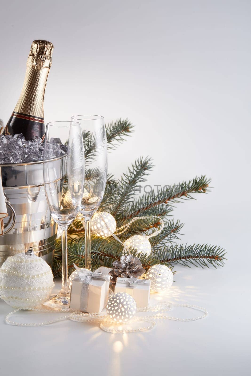 Still life with cooled champagne bottle standing in a bucket with ice, two champagne flutes and Christmas ornaments on a gray background, Christmas and New Year celebration