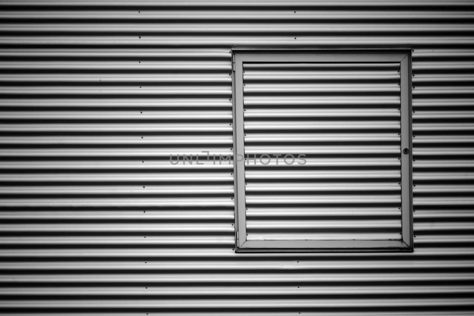 The closeup of the corrugated iron facade of an industrial building with a metal window frame..