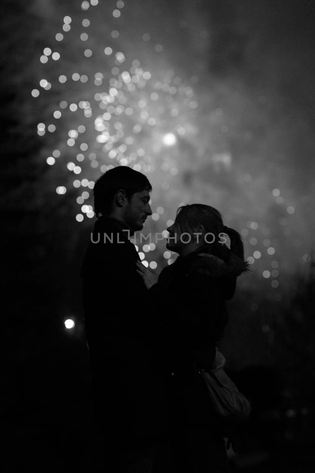 A silhouette of a kissing couple in front of a huge fireworks display. Filtered black and white image with grain