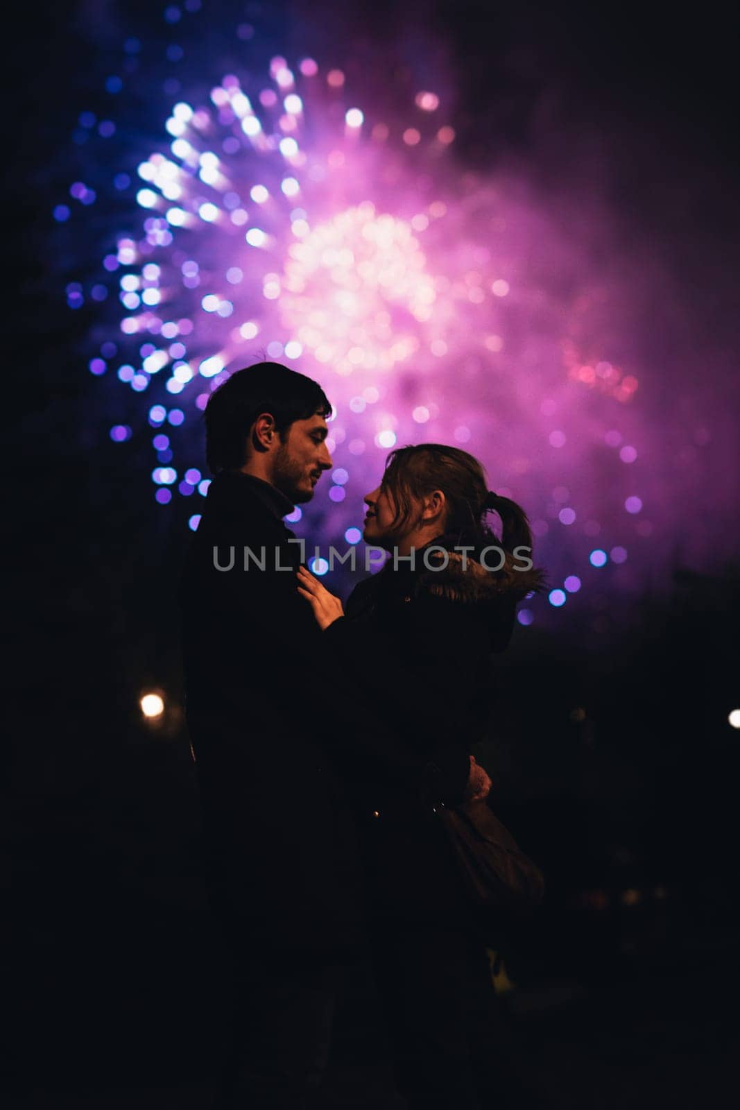 A silhouette of a kissing couple in front of a huge fireworks display. Filtered image with grain