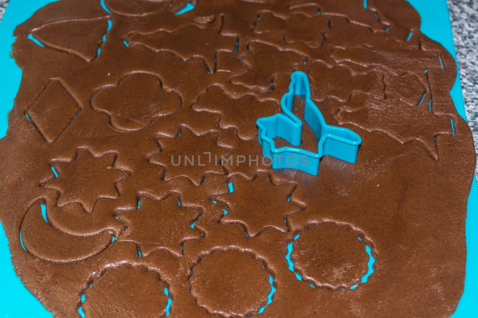 Raw dough is being punched out for the holiday cookies on a blue underlay. Preparing gingerbread cookies. Steps to making biscuits. Top view.
