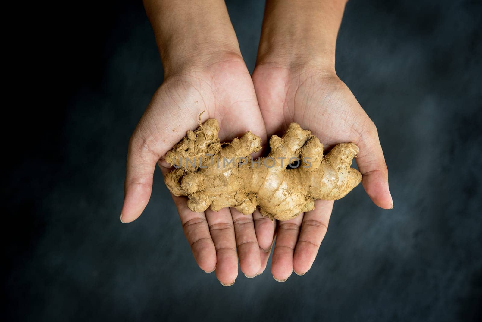 Ginger in hands on dark background, top view.